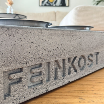 Eingegossener Hundename im grauen Beton, Nahaufnahme der Personalisierung mit sichtbarer Betonstruktur