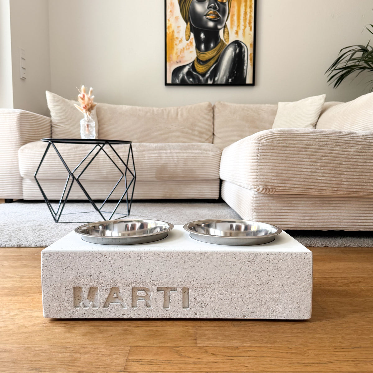 Napfhalter aus hellem Beton mit personalisiertem Namen und zwei Edelstahlnäpfen, frontal im Wohnraum